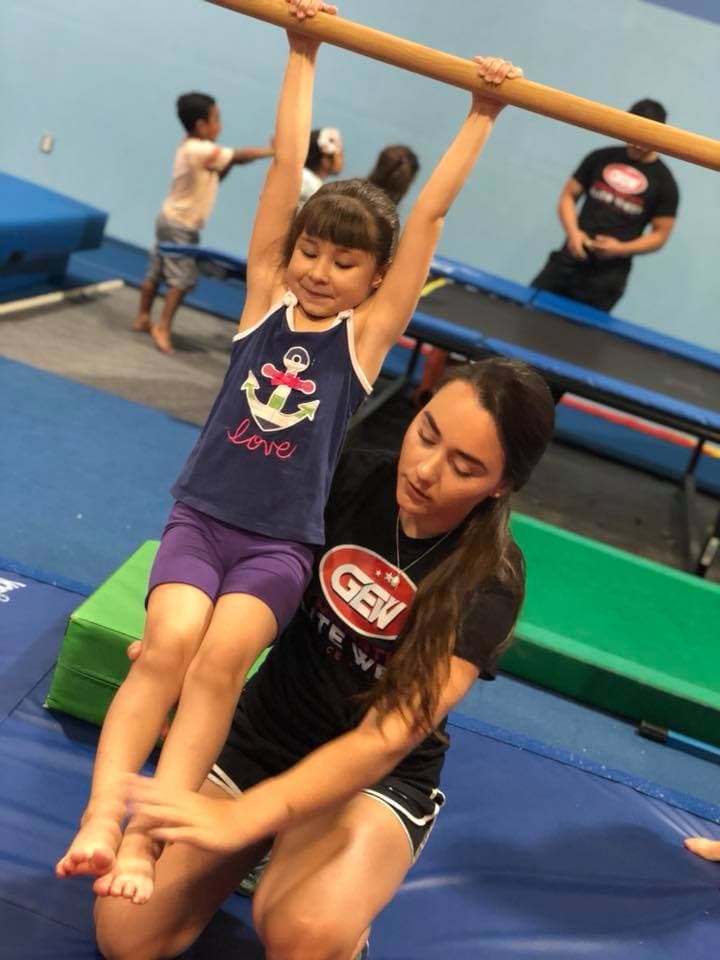 Coach spotting a young gymnast on the bar at El Paso Gymnastics